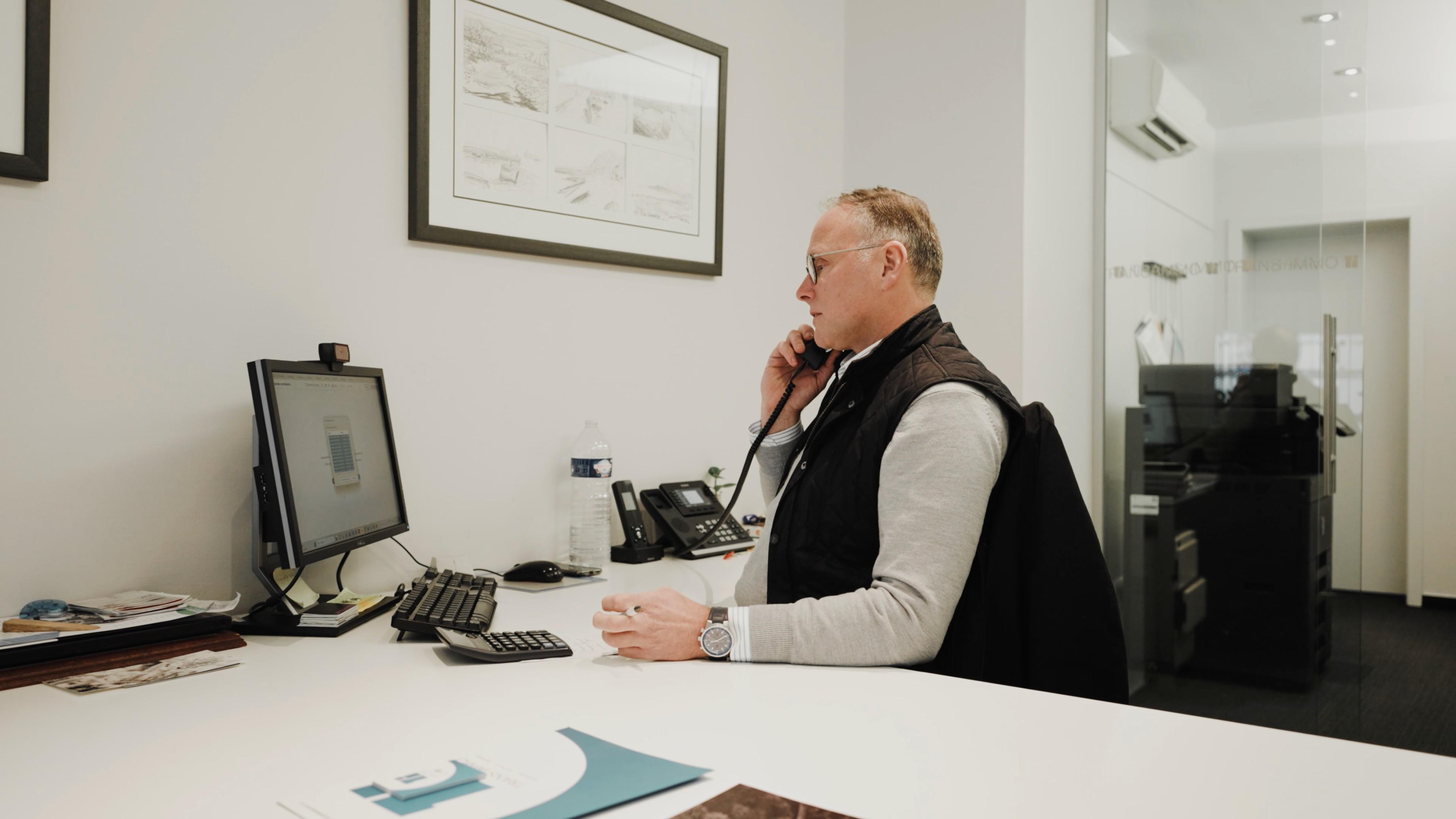 Persoon doet een telefoongesprek en zit achter een bureau